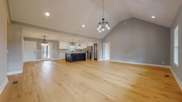 unfurnished living room with a notable chandelier, high vaulted ceiling, and light hardwood / wood-style flooring