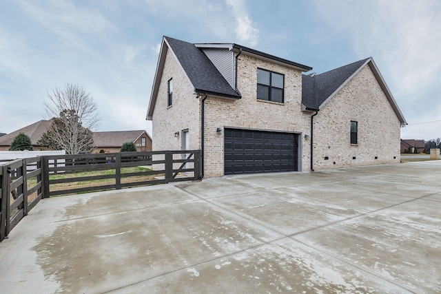 view of property exterior featuring an attached garage, brick siding, fence, concrete driveway, and roof with shingles