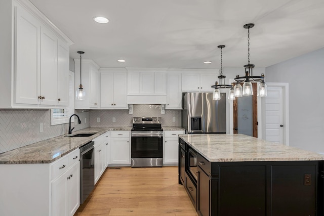 kitchen featuring white cabinets, a kitchen island, appliances with stainless steel finishes, light wood-style floors, and a sink