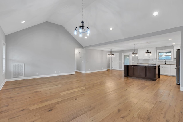 unfurnished living room featuring light wood-type flooring, baseboards, visible vents, and a notable chandelier