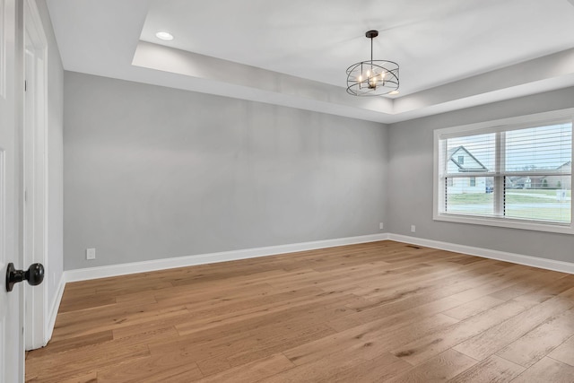 spare room featuring light wood-type flooring, baseboards, a chandelier, and a tray ceiling