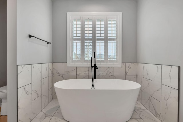 full bathroom with toilet, marble finish floor, plenty of natural light, and a soaking tub