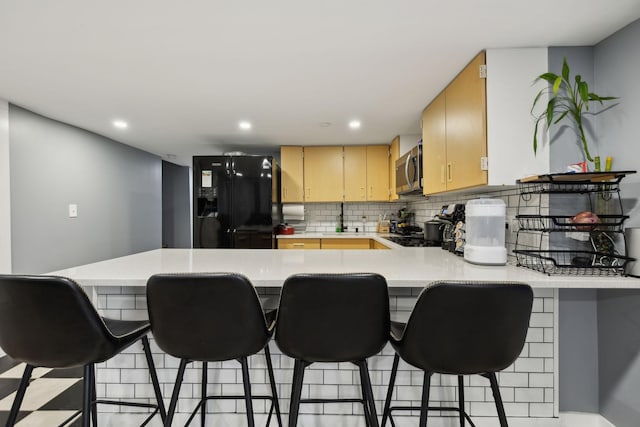 kitchen featuring black refrigerator, tasteful backsplash, a kitchen bar, kitchen peninsula, and light brown cabinets