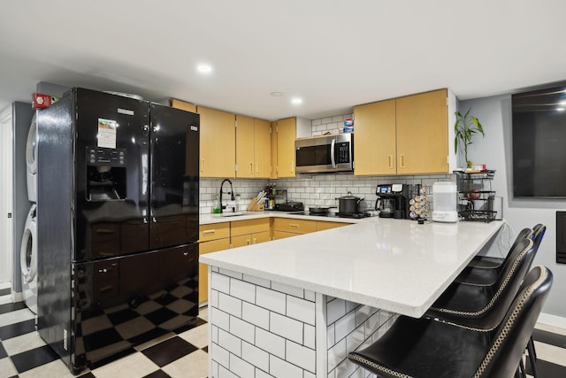 kitchen featuring light brown cabinetry, black appliances, kitchen peninsula, and a kitchen bar