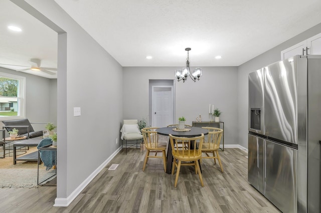 dining area with ceiling fan with notable chandelier and light wood-type flooring