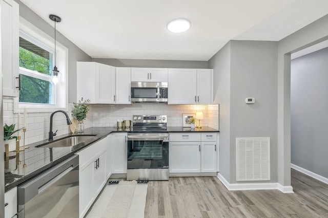 kitchen with white cabinetry, stainless steel appliances, sink, and pendant lighting