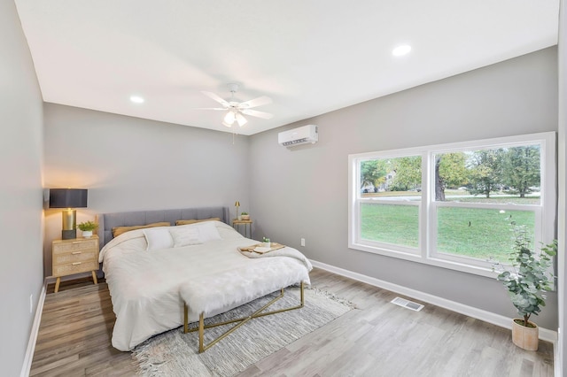 bedroom featuring hardwood / wood-style flooring, a wall mounted air conditioner, and ceiling fan