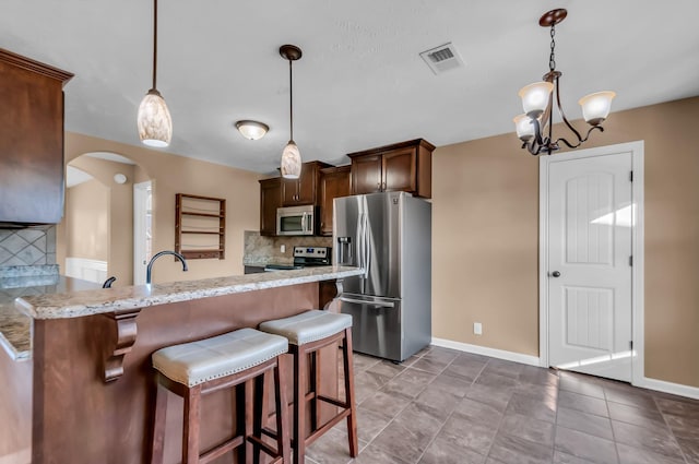 kitchen featuring appliances with stainless steel finishes, decorative light fixtures, a kitchen breakfast bar, kitchen peninsula, and light stone countertops