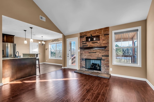 unfurnished living room featuring lofted ceiling, sink, an inviting chandelier, dark hardwood / wood-style flooring, and a stone fireplace