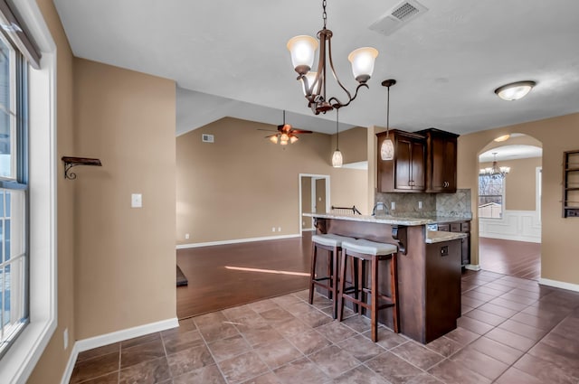 kitchen featuring ceiling fan with notable chandelier, a kitchen breakfast bar, hanging light fixtures, dark brown cabinetry, and light stone counters