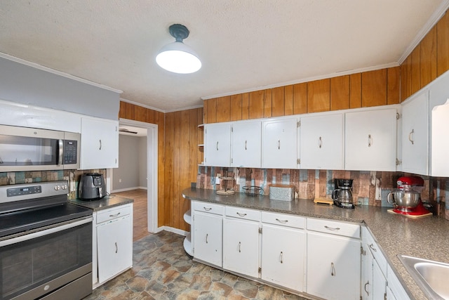 kitchen with white cabinetry, wooden walls, ornamental molding, and appliances with stainless steel finishes