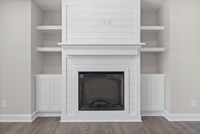 room details featuring a glass covered fireplace, baseboards, and wood finished floors