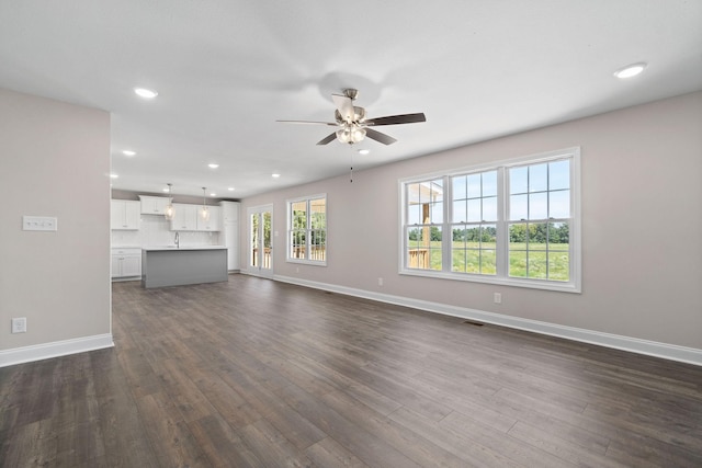 unfurnished living room with dark wood-style flooring, recessed lighting, a sink, and baseboards