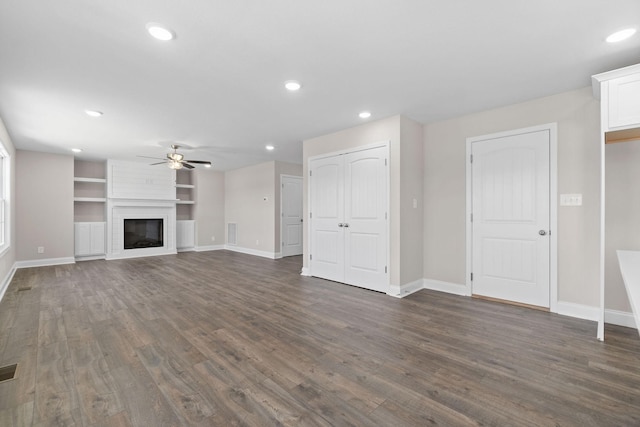 unfurnished living room with ceiling fan, a large fireplace, dark hardwood / wood-style flooring, and built in shelves