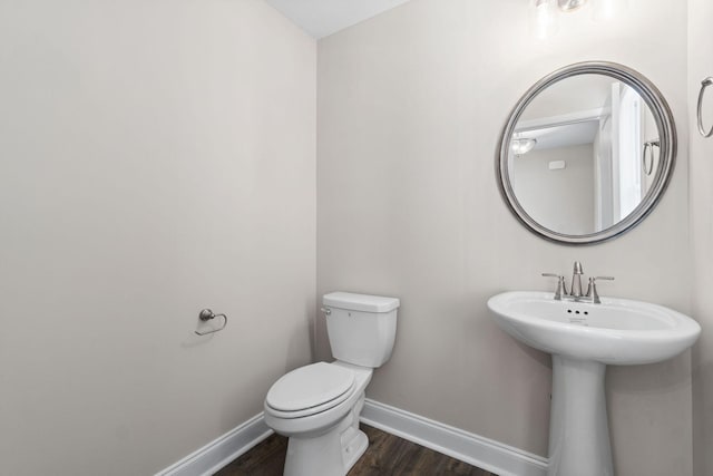 half bathroom featuring toilet, a sink, baseboards, and wood finished floors