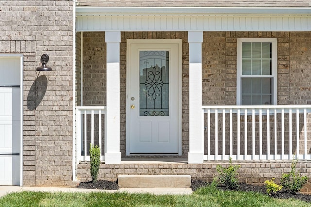 view of exterior entry featuring a garage, a porch, and brick siding