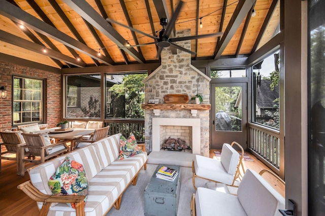 sunroom featuring an outdoor stone fireplace, vaulted ceiling with beams, wood ceiling, and ceiling fan