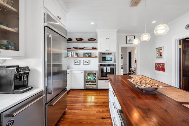 kitchen featuring appliances with stainless steel finishes, butcher block counters, wine cooler, white cabinets, and hanging light fixtures