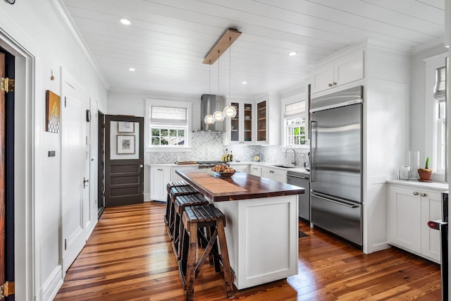 kitchen featuring a kitchen island, wood counters, a kitchen bar, stainless steel appliances, and wall chimney range hood