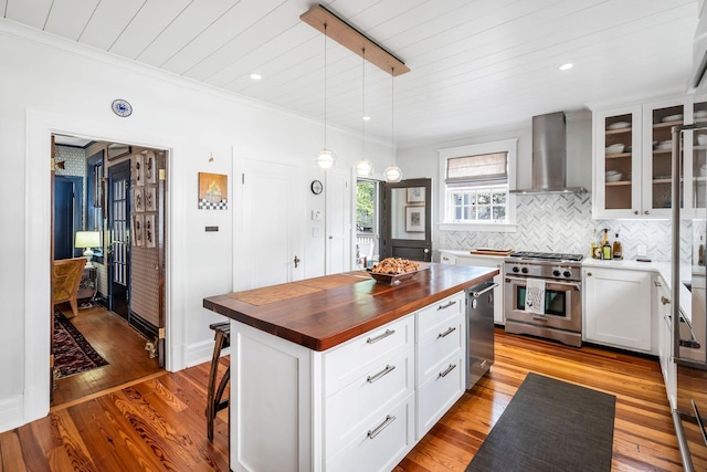 kitchen with pendant lighting, wall chimney range hood, high end stainless steel range oven, a center island, and white cabinets