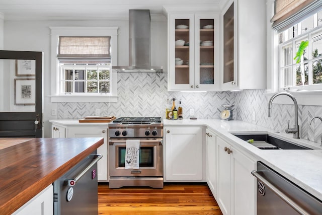 kitchen featuring butcher block countertops, sink, appliances with stainless steel finishes, white cabinets, and wall chimney exhaust hood