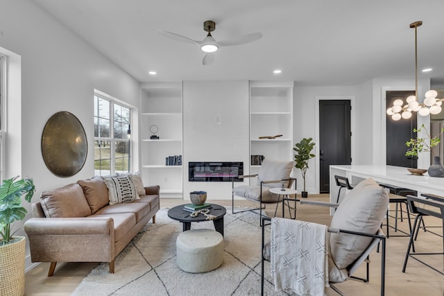 living room featuring ceiling fan with notable chandelier, built in shelves, and light wood-type flooring