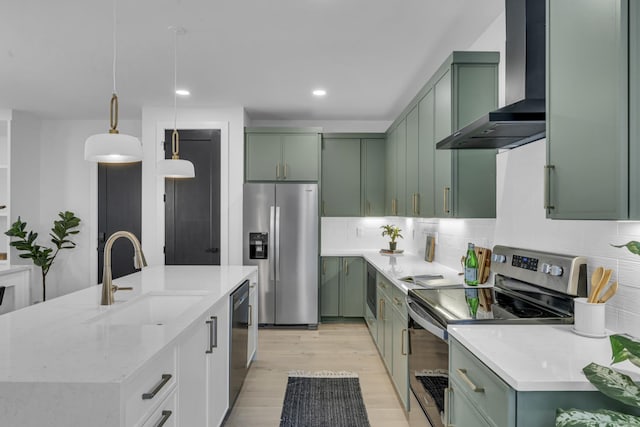 kitchen with sink, green cabinets, pendant lighting, stainless steel appliances, and wall chimney range hood