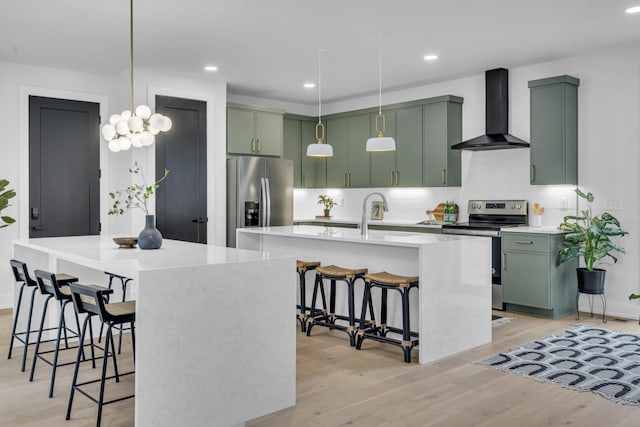 kitchen with stainless steel appliances, green cabinets, a center island with sink, and wall chimney range hood