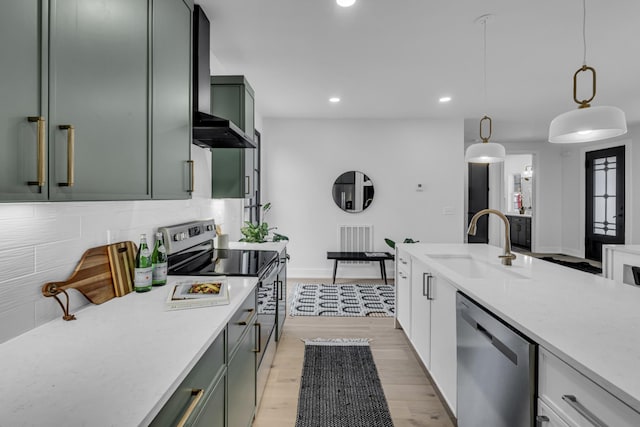 kitchen with sink, hanging light fixtures, stainless steel appliances, wall chimney range hood, and light hardwood / wood-style flooring