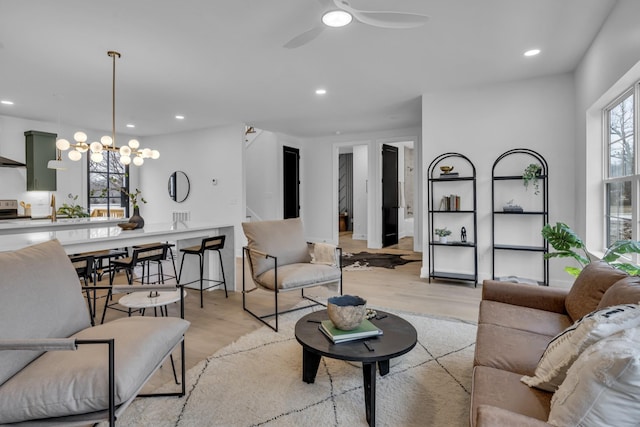 living room featuring ceiling fan with notable chandelier and light wood-type flooring