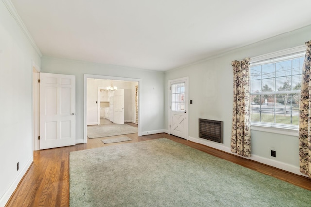 unfurnished living room featuring heating unit, a notable chandelier, wood-type flooring, and ornamental molding