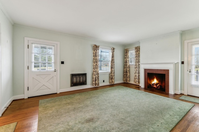 unfurnished living room with heating unit, ornamental molding, hardwood / wood-style floors, and a brick fireplace