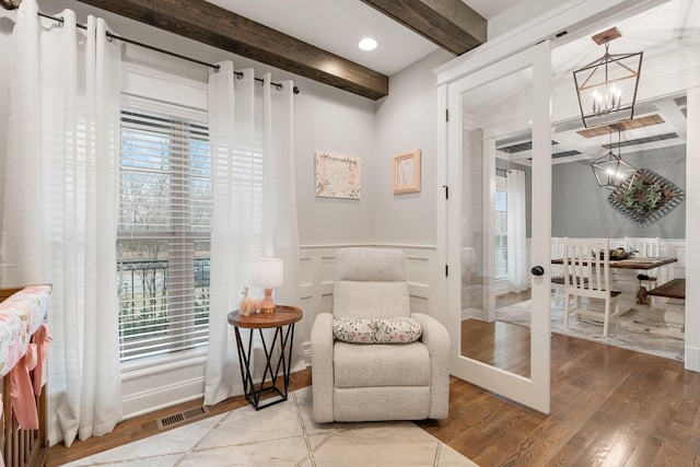 living area featuring a notable chandelier, a wealth of natural light, hardwood / wood-style floors, and beamed ceiling