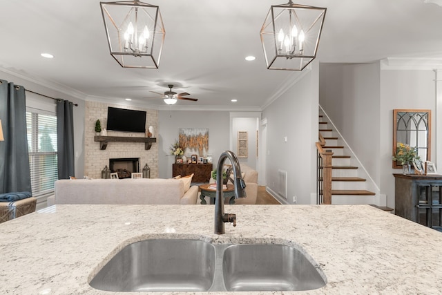 kitchen with light stone counters, sink, hanging light fixtures, and a brick fireplace