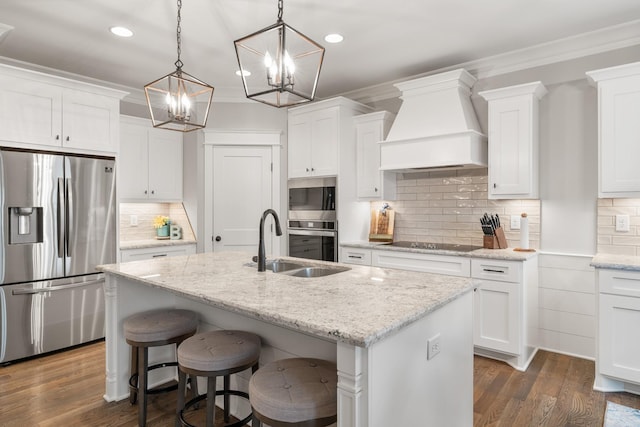 kitchen with appliances with stainless steel finishes, a kitchen island with sink, custom range hood, and white cabinets