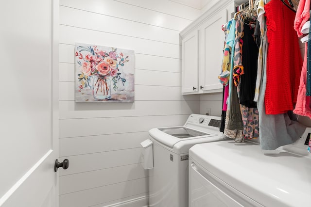 clothes washing area featuring cabinets, washing machine and clothes dryer, and wood walls