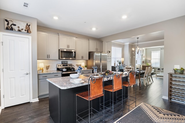 kitchen with a breakfast bar area, gray cabinets, hanging light fixtures, stainless steel appliances, and light stone countertops