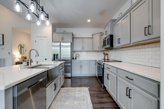 kitchen featuring appliances with stainless steel finishes, a kitchen island with sink, gray cabinetry, and decorative backsplash