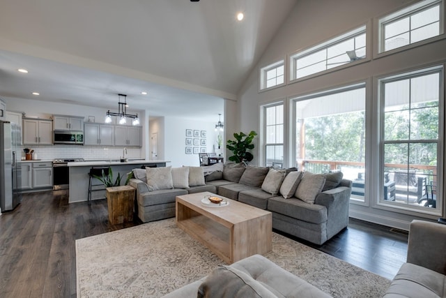 living room with high vaulted ceiling, sink, a notable chandelier, and dark hardwood / wood-style flooring