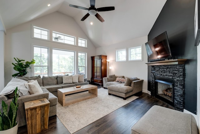 living room featuring dark wood-type flooring, ceiling fan, a stone fireplace, and high vaulted ceiling