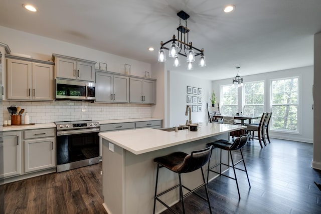 kitchen with sink, hanging light fixtures, a center island with sink, appliances with stainless steel finishes, and decorative backsplash