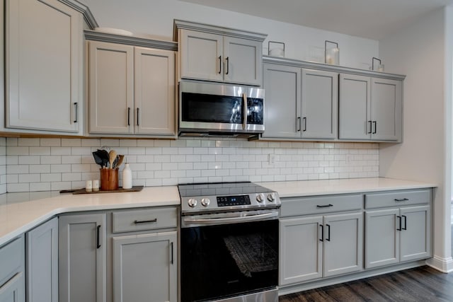 kitchen with appliances with stainless steel finishes, dark hardwood / wood-style floors, gray cabinetry, and backsplash