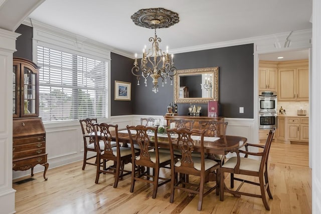 dining space with arched walkways, crown molding, a notable chandelier, light wood-style flooring, and wainscoting