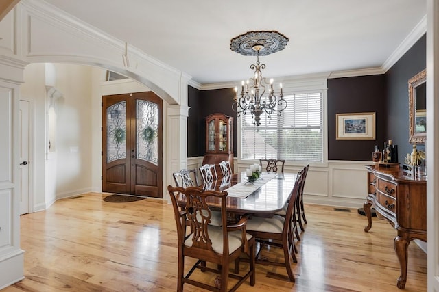 dining room featuring light wood finished floors, arched walkways, an inviting chandelier, crown molding, and a decorative wall