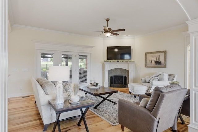 living room with a fireplace, a ceiling fan, baseboards, light wood finished floors, and crown molding