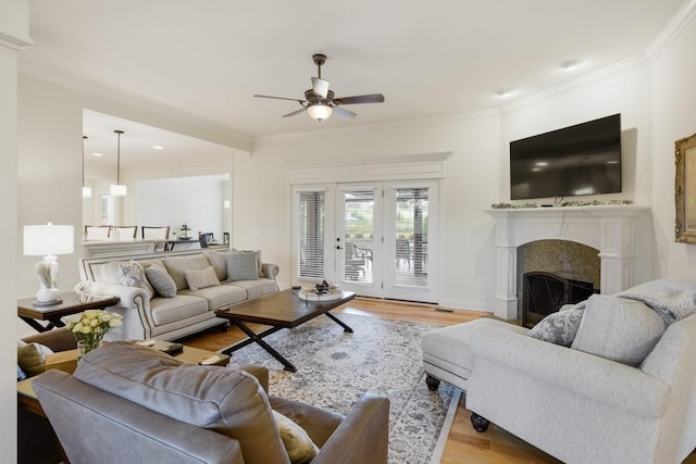 living area featuring light wood finished floors, a premium fireplace, a ceiling fan, and crown molding