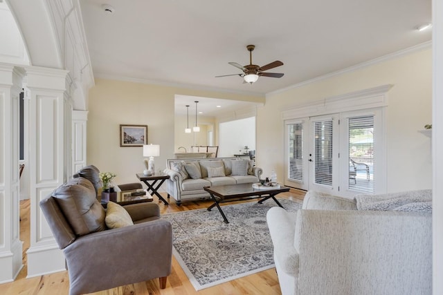 living area with light wood-type flooring, crown molding, decorative columns, and ceiling fan