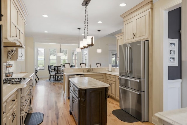 kitchen with appliances with stainless steel finishes, hanging light fixtures, a peninsula, light countertops, and a sink