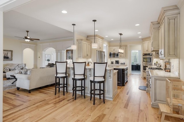 kitchen with appliances with stainless steel finishes, pendant lighting, tasteful backsplash, a kitchen breakfast bar, and light hardwood / wood-style floors