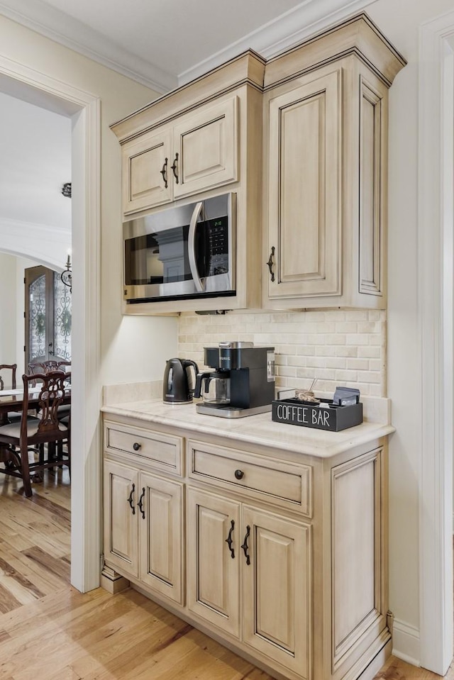 bar with ornamental molding, stainless steel microwave, backsplash, and light wood-style flooring